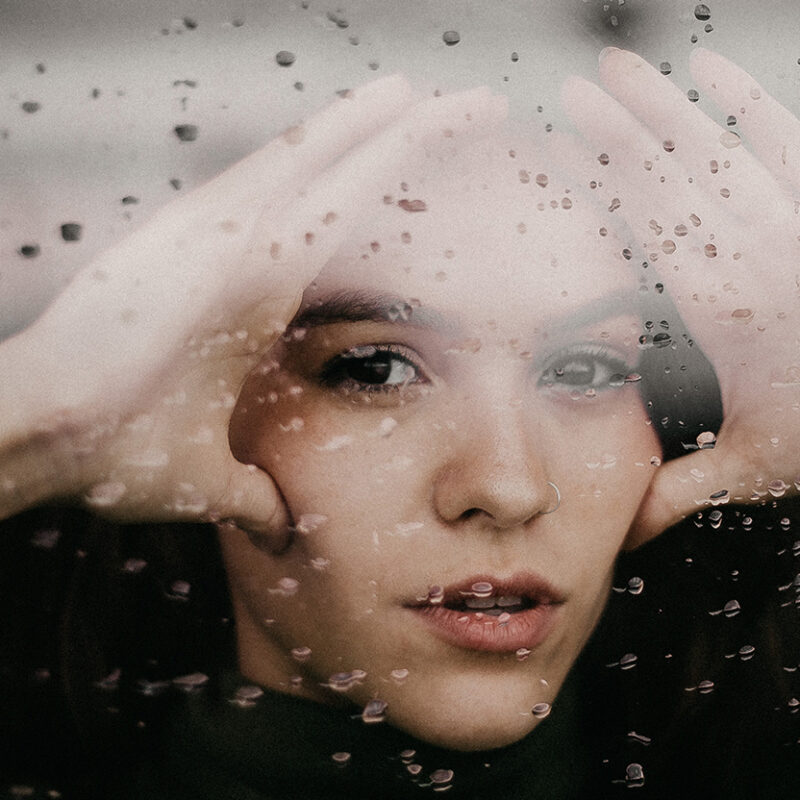 Nainen katselee läpi sateen täplittämän ikkunan