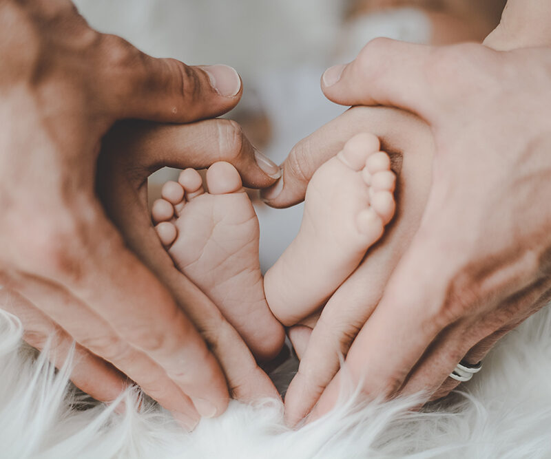Vanhempien kädet muodostavat sydämen pienen vauvan varpaiden ympärille.