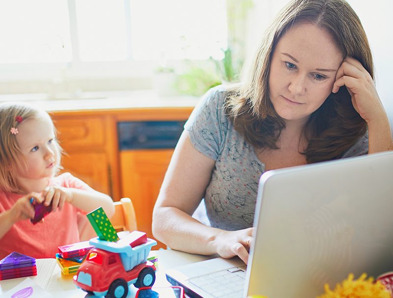 Opiskeleva äiti kannettavan tietokoneen ääressä lapsi katsoo vieressä