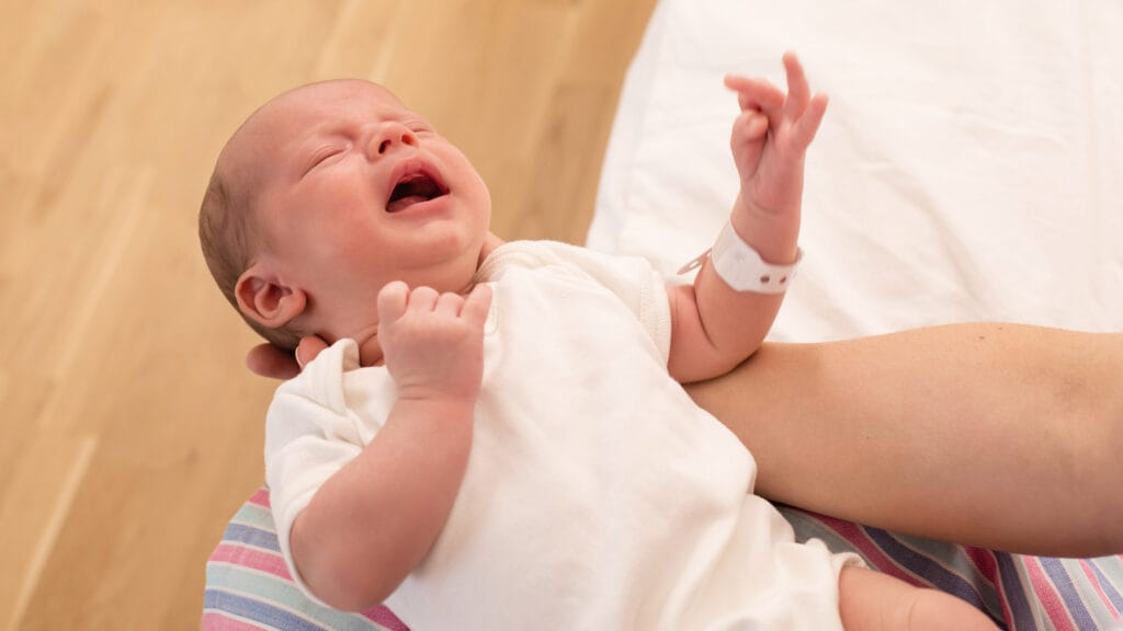 Vastasyntynyt vauva itkee äidin käsivarsilla.