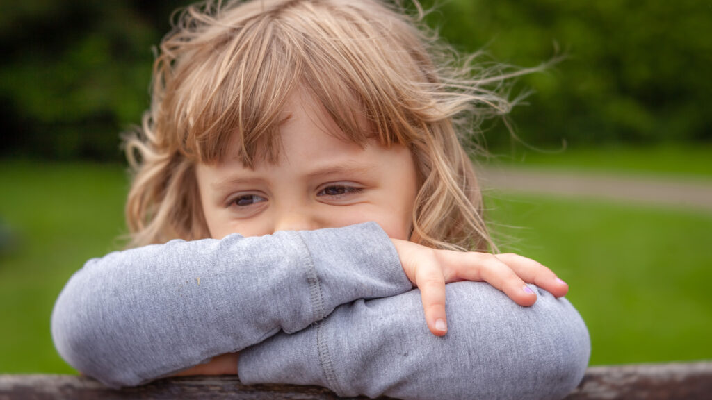 Ruskeatukkainen surullinen alle kouluikäinen tyttö nojaa käsiinsä.