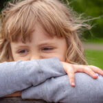 Ruskeatukkainen surullinen alle kouluikäinen tyttö nojaa käsiinsä.