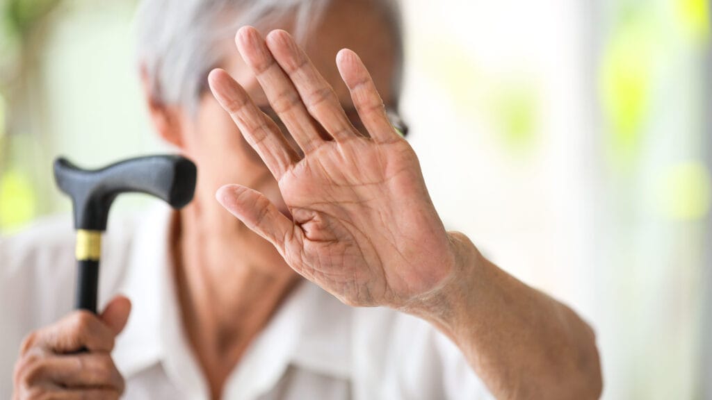 Ikääntynyt nainen on nostanut käden kasvojensa suojaksi.