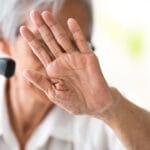 Ikääntynyt nainen on nostanut käden kasvojensa suojaksi.