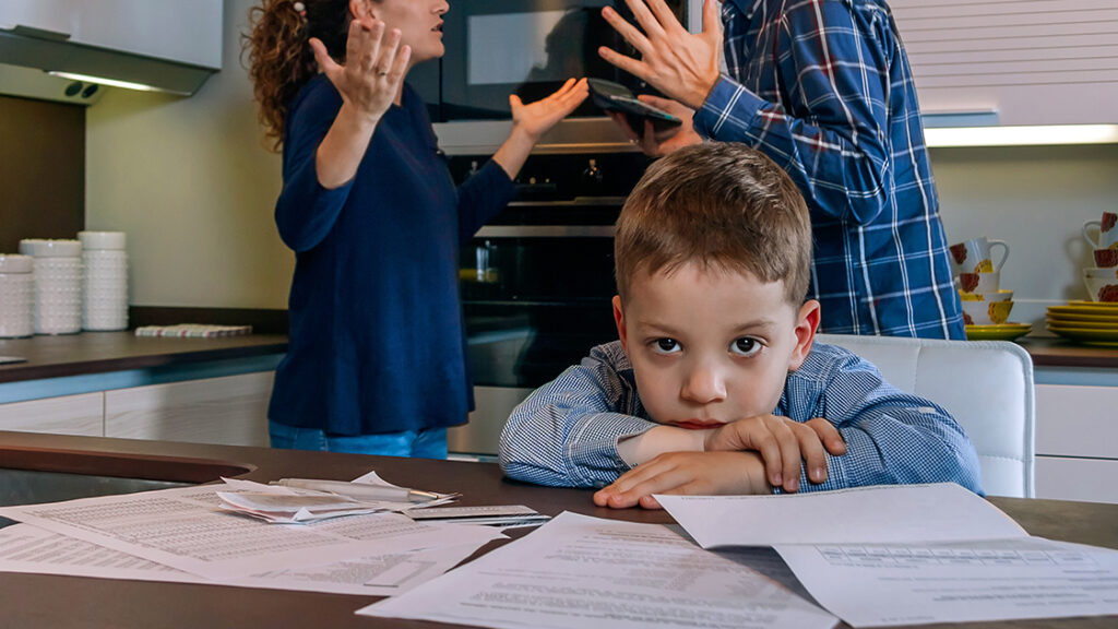Surullinen poika katselee kameraan vanhempien riidellessä taustalla.