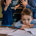 Surullinen poika katselee kameraan vanhempien riidellessä taustalla.